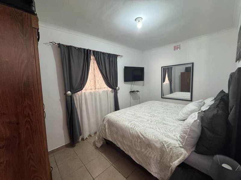 A functional bedroom featuring tiled flooring, neutral walls, and a ceiling vent, providing a simple and practical living space.