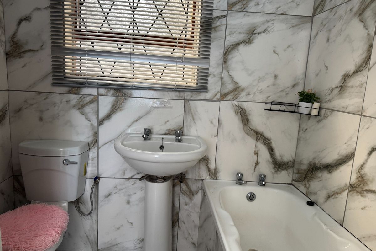 A functional bathroom featuring marble-effect wall tiling, a pedestal washbasin, a standard toilet, and a bathtub with chrome fixtures.