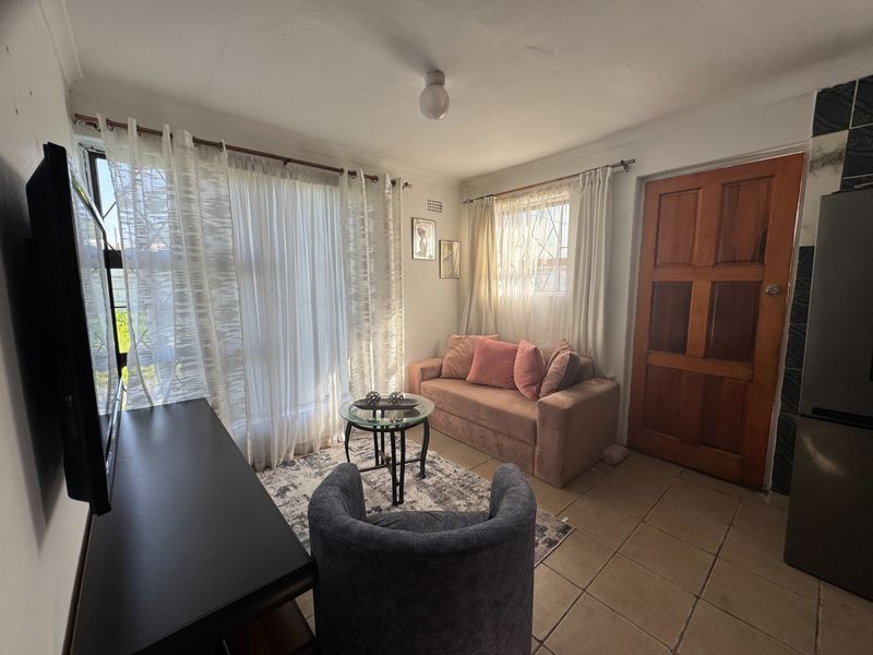 A compact living area featuring tiled flooring, a solid timber door, and natural light through large windows.