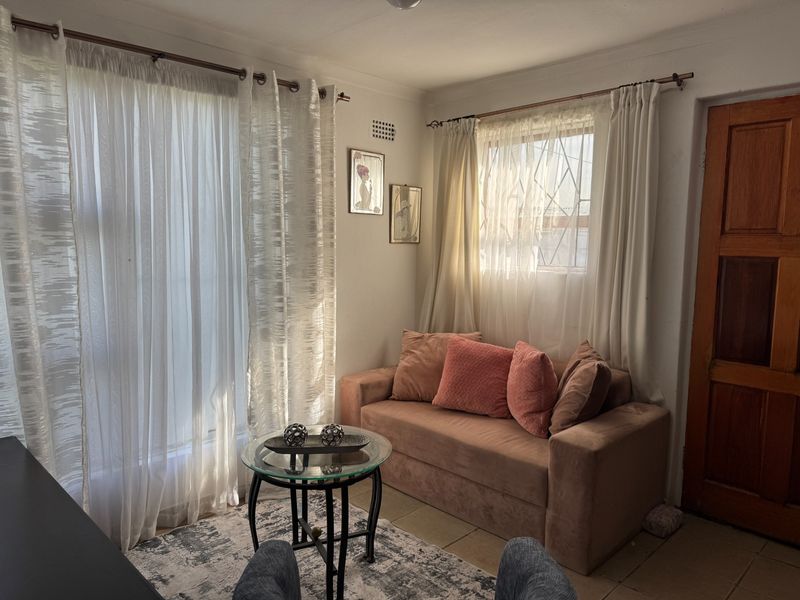 A cozy living area featuring tiled flooring, natural light through large windows, and a solid timber door.