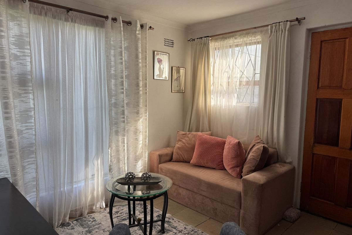 A cozy living area featuring tiled flooring, natural light through large windows, and a solid timber door.
