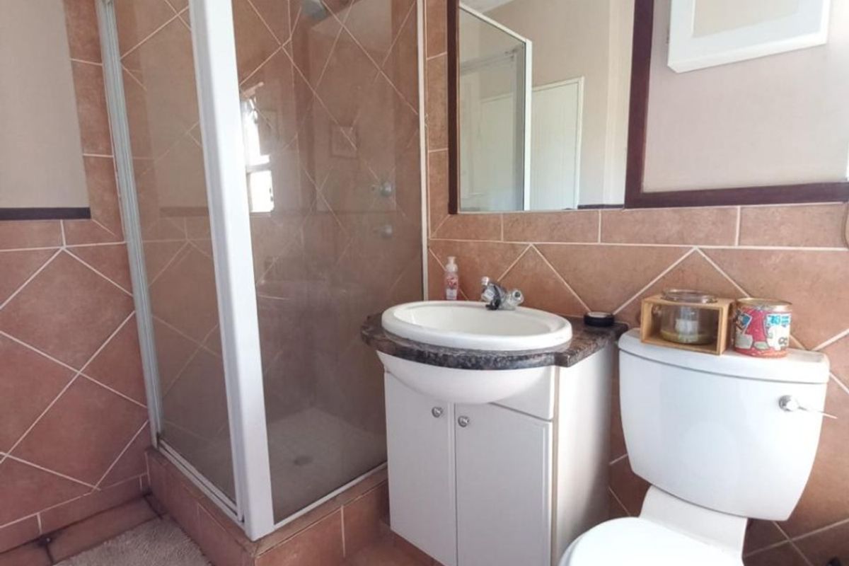 A functional bathroom featuring a corner shower enclosure, vanity cabinet with integrated basin, toilet, and neutral tiled finishes.