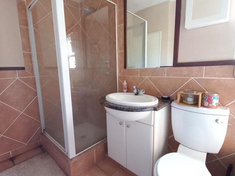 A functional bathroom featuring a corner shower enclosure, vanity cabinet with integrated basin, toilet, and neutral tiled finishes.