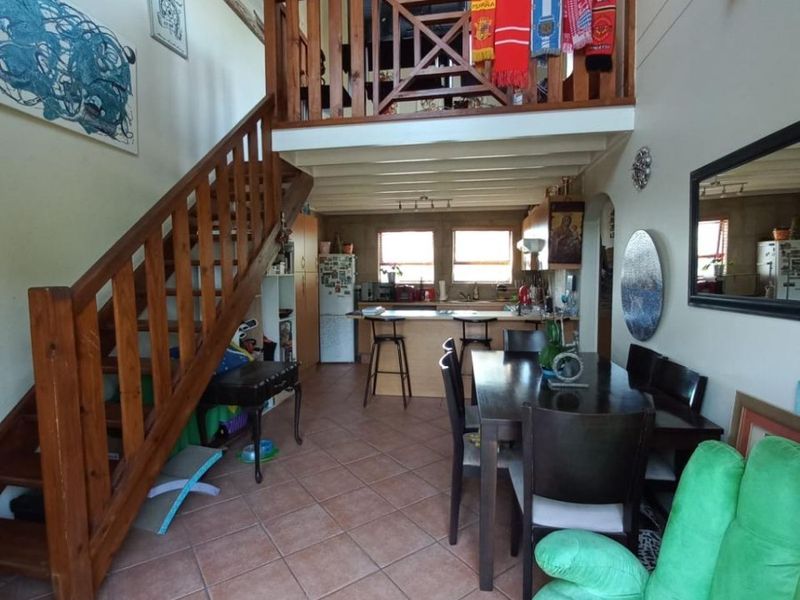 Open-plan living and kitchen area featuring a wooden staircase leading to a mezzanine level, tiled flooring, and a functional kitchen layout.