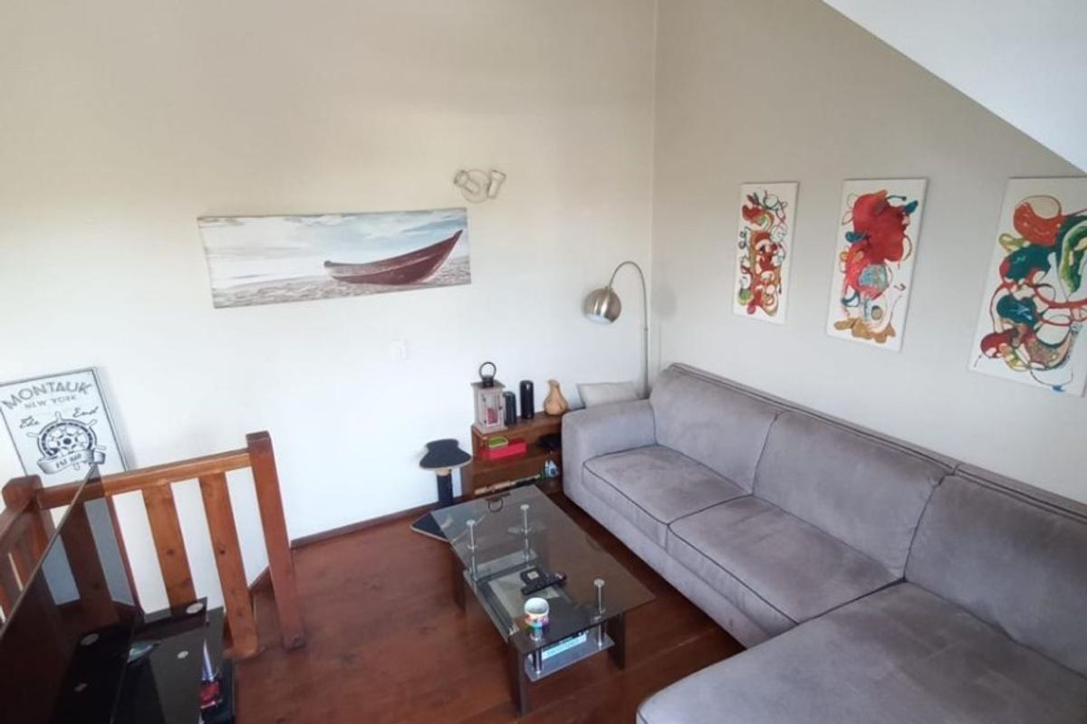 A cozy living room featuring warm wooden flooring, a unique sloped ceiling, and a wooden staircase railing, creating a comfortable and inviting atmosphere.