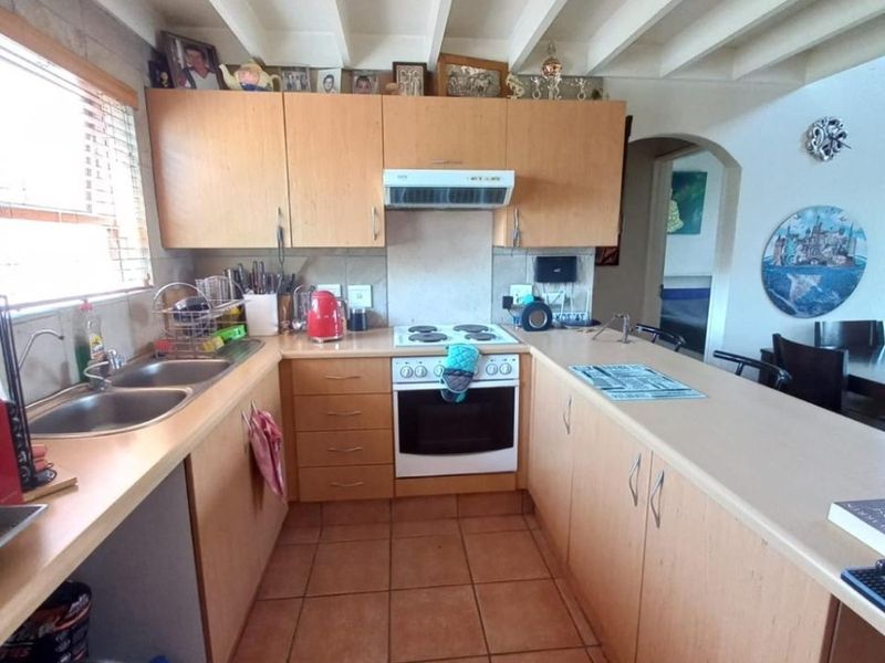 A functional kitchen featuring light wood cabinetry, a double bowl sink, electric stove with extractor, and a breakfast bar with tiled flooring.