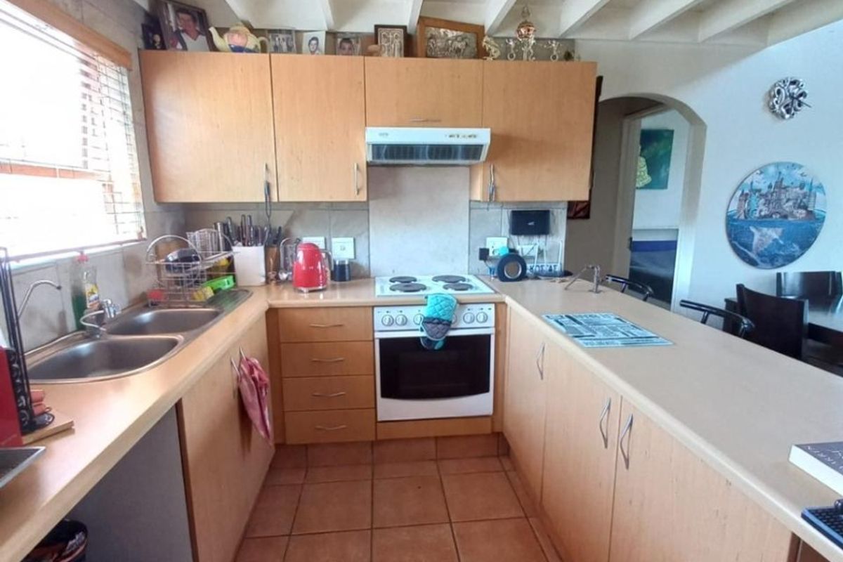 A functional kitchen featuring light wood cabinetry, a double bowl sink, electric stove with extractor, and a breakfast bar with tiled flooring.