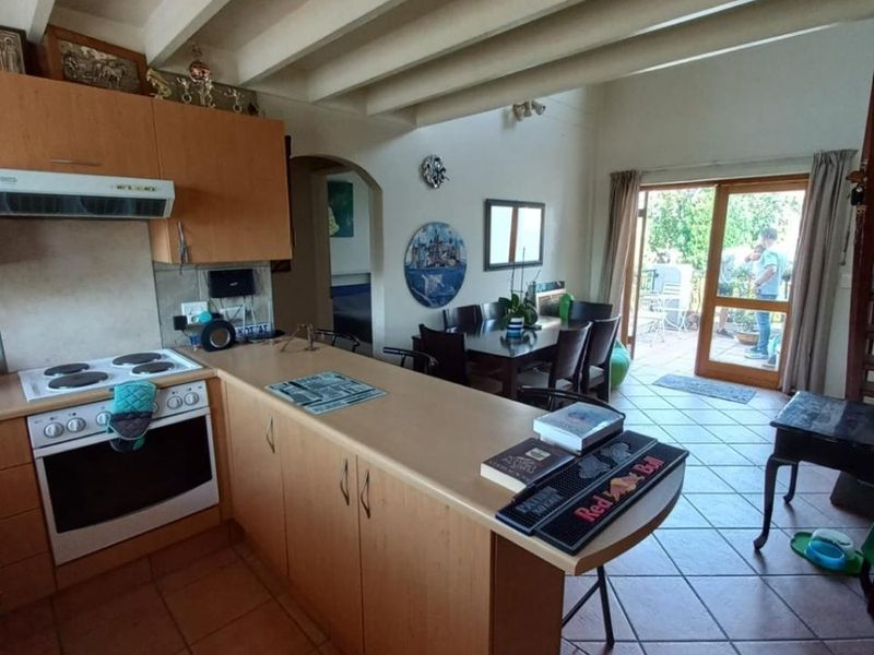 Open-plan kitchen and dining area featuring exposed ceiling beams, tiled flooring, and direct access to an outdoor patio through a sliding glass door.