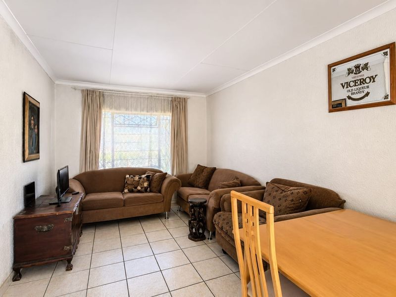 A functional living room featuring tiled flooring, coved ceilings, and a window fitted with a security gate.