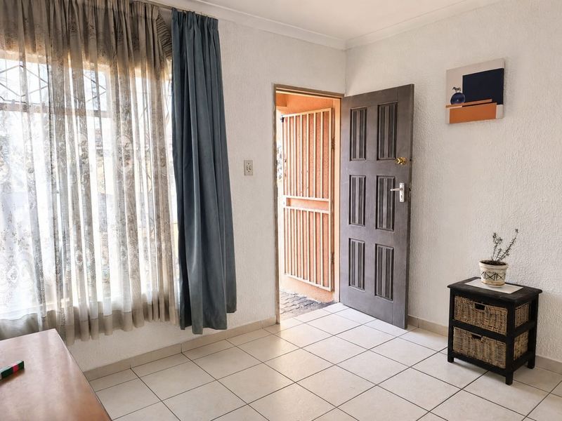 A bright entry area featuring tiled flooring, a secure entrance door with a security gate, and large windows allowing natural light.