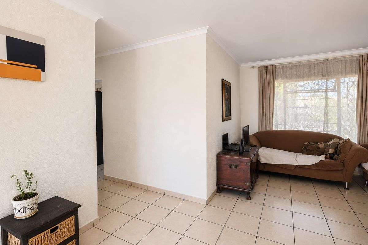 A bright living room featuring neutral ceramic floor tiles, coved cornicing, and a large window fitted with a security gate.