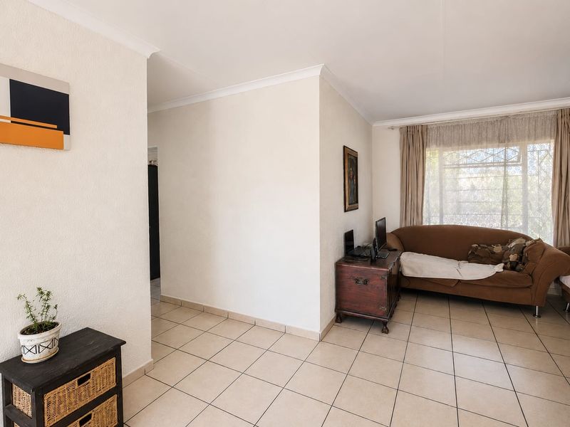 A bright living room featuring neutral ceramic floor tiles, coved cornicing, and a large window fitted with a security gate.