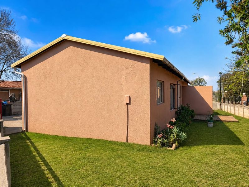 A view of the rear exterior of the house featuring plastered walls, a pitched roof, and a small paved patio area set within a garden.