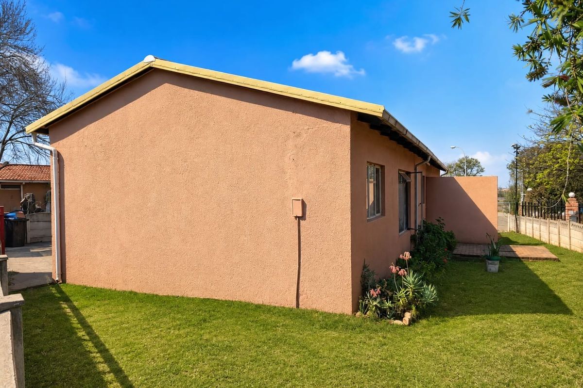 A view of the rear exterior of the house featuring plastered walls, a pitched roof, and a small paved patio area set within a garden.