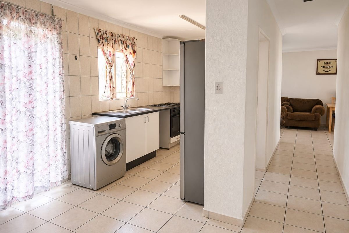 A functional kitchen area featuring tiled flooring, built-in cabinetry, a stainless steel sink, and integrated cooking appliances, flowing into an adjacent living space.