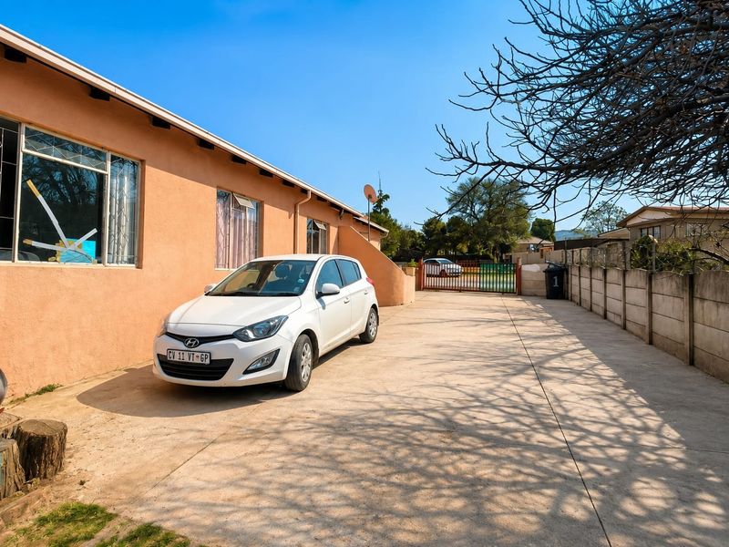 Front exterior view of the property featuring a concrete driveway, secure boundary walling, and metal gate access.