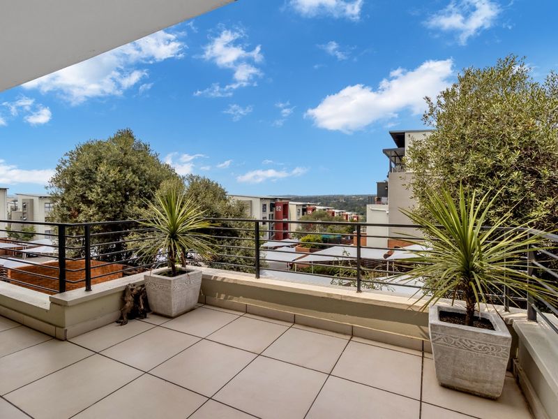 A spacious covered balcony featuring tiled flooring and metal railings, offering an elevated view of the surrounding residential complex.