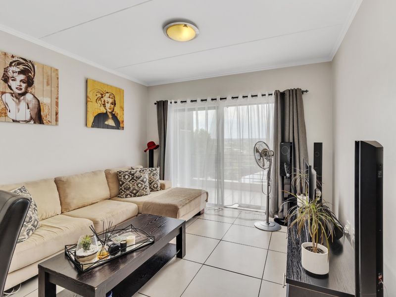 A well-lit living room featuring tiled flooring and a large sliding glass door providing access to an outdoor balcony area.