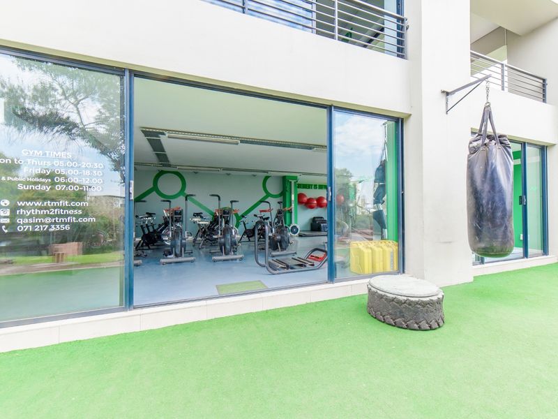 A ground-level gym facility featuring large sliding glass doors, artificial turf flooring, and an outdoor training area with a punching bag.