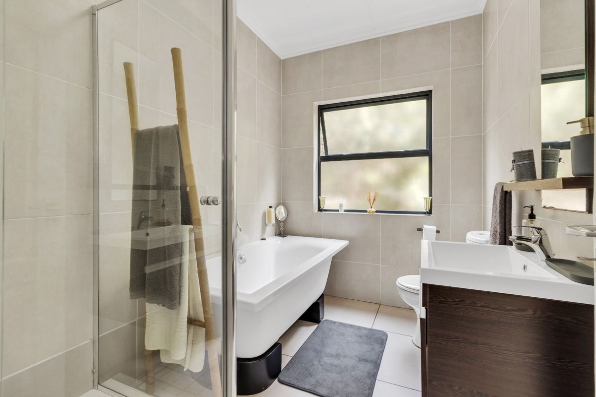 Modern bathroom featuring a freestanding bathtub, glass-enclosed shower, vanity with basin, and neutral floor-to-ceiling tiling.