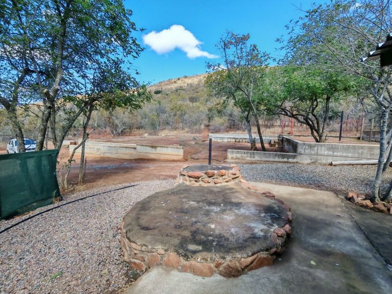 An expansive outdoor garden area featuring a stone-clad fire pit, concrete retaining walls, and natural landscape views, offering significant potential for landscaping and development.