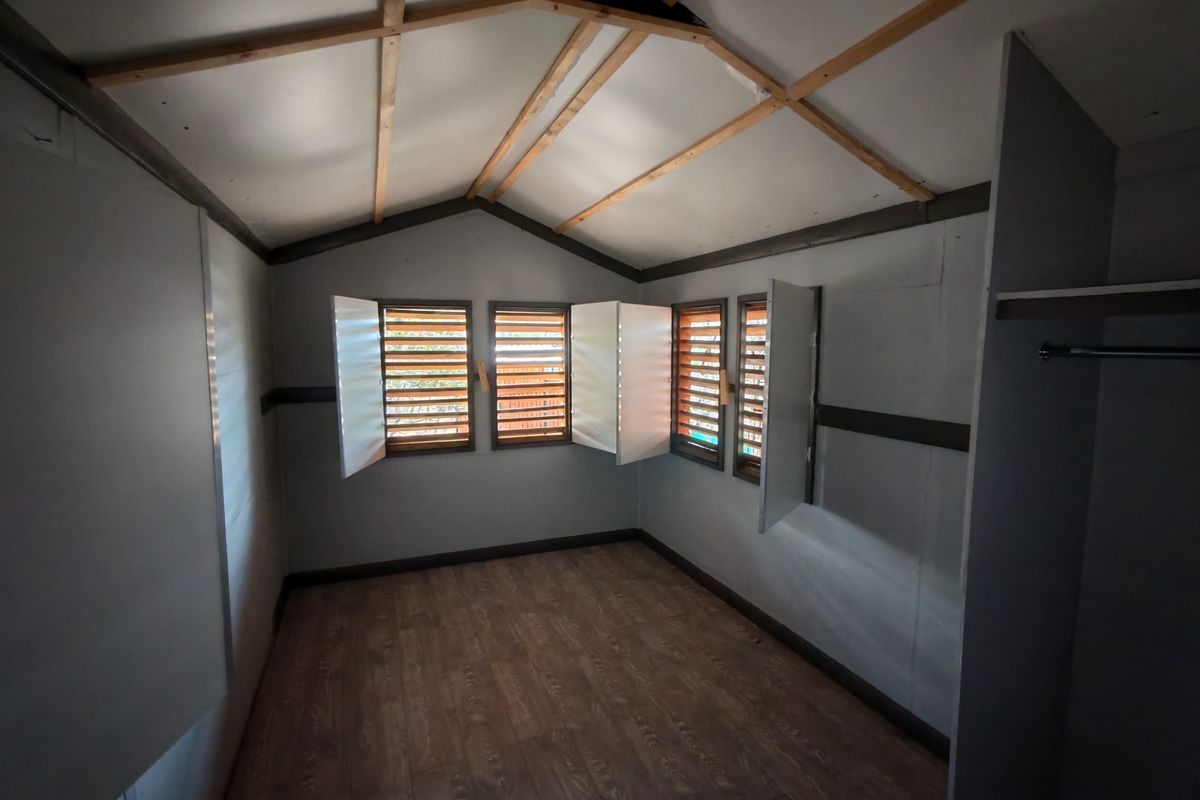 An empty bedroom featuring exposed timber rafters, louvered window shutters, and laminate flooring, offering a blank canvas for interior design.