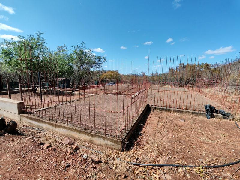 An outdoor construction site showing a concrete foundation slab with exposed reinforcing steel bars, indicating an incomplete building project.