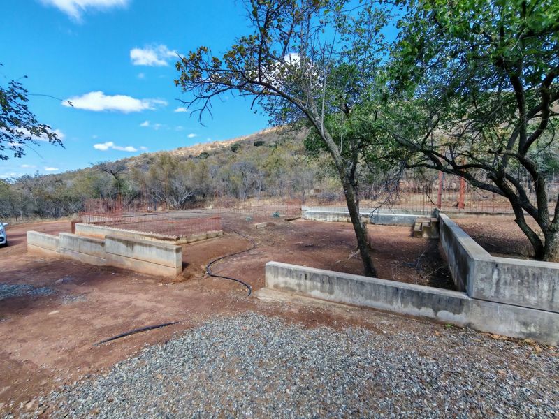 An outdoor area showing the early stages of construction with concrete retaining walls and exposed foundation reinforcement bars set against a natural landscape.