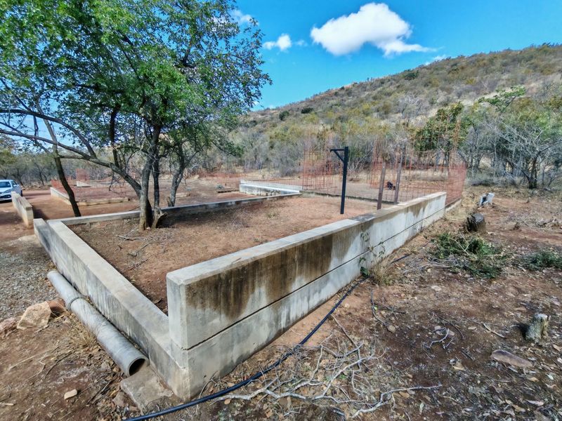 An outdoor area featuring concrete retaining walls and foundation work, set against a natural hillside landscape.