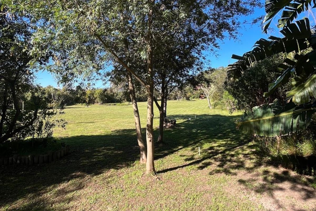 A spacious, well-maintained residential garden area featuring mature trees and open lawn space, offering a peaceful outdoor setting.