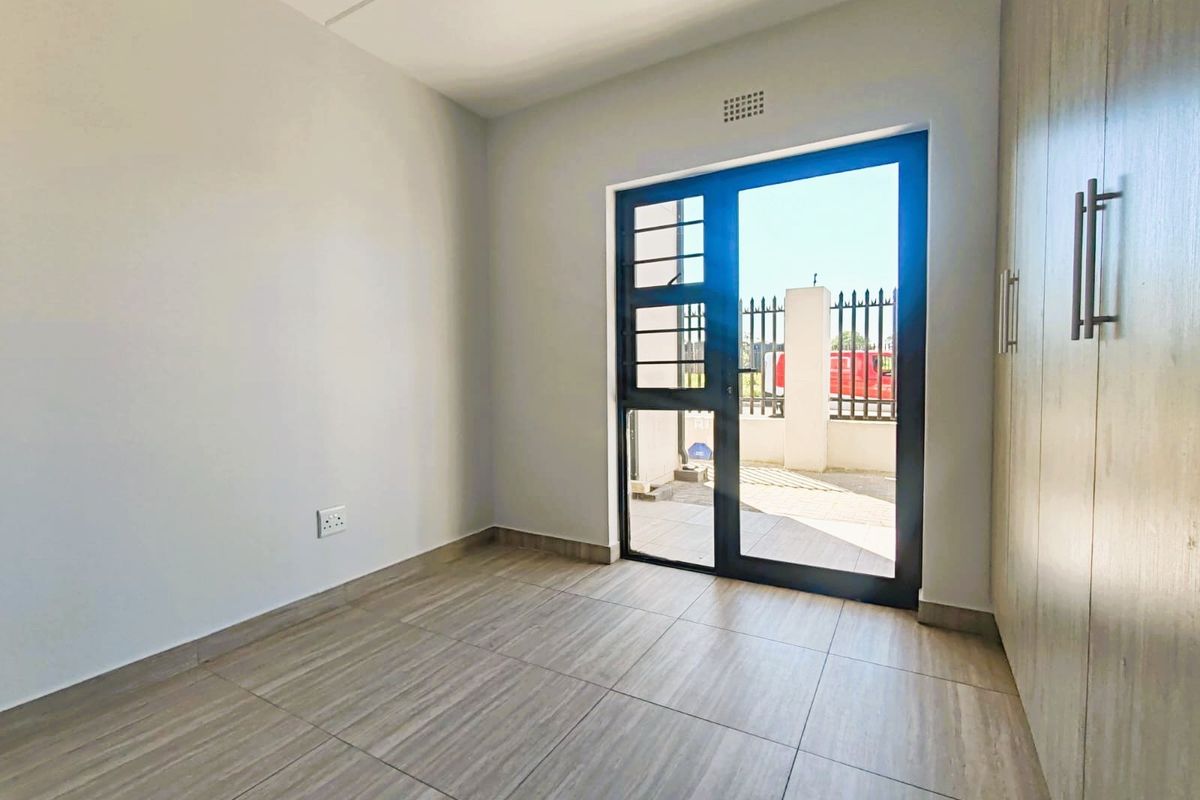 A bright, empty bedroom featuring modern tiled flooring, built-in cupboards, and a glass door providing direct access to the exterior.