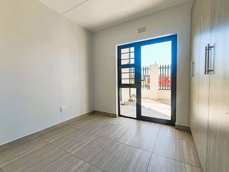 A bright, empty bedroom featuring modern tiled flooring, built-in cupboards, and a glass door providing direct access to the exterior.