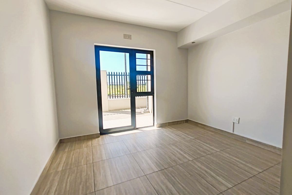 A bright, empty living area featuring modern tiled flooring and a glass door providing direct access to an outdoor space.