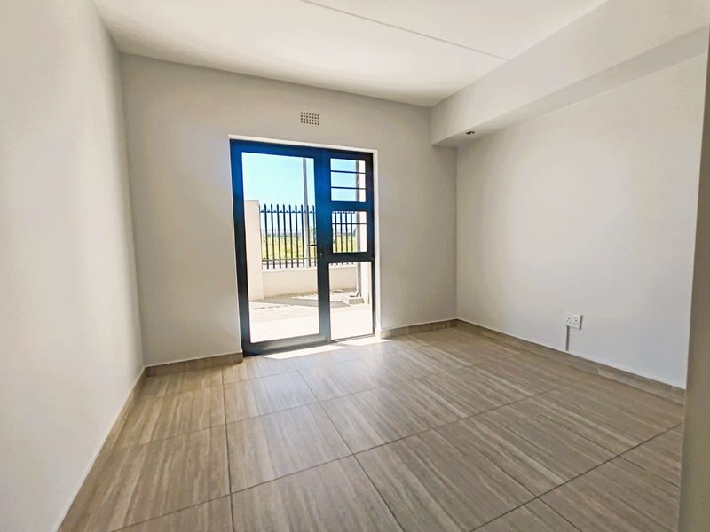 A bright, empty living area featuring modern tiled flooring and a glass door providing direct access to an outdoor space.