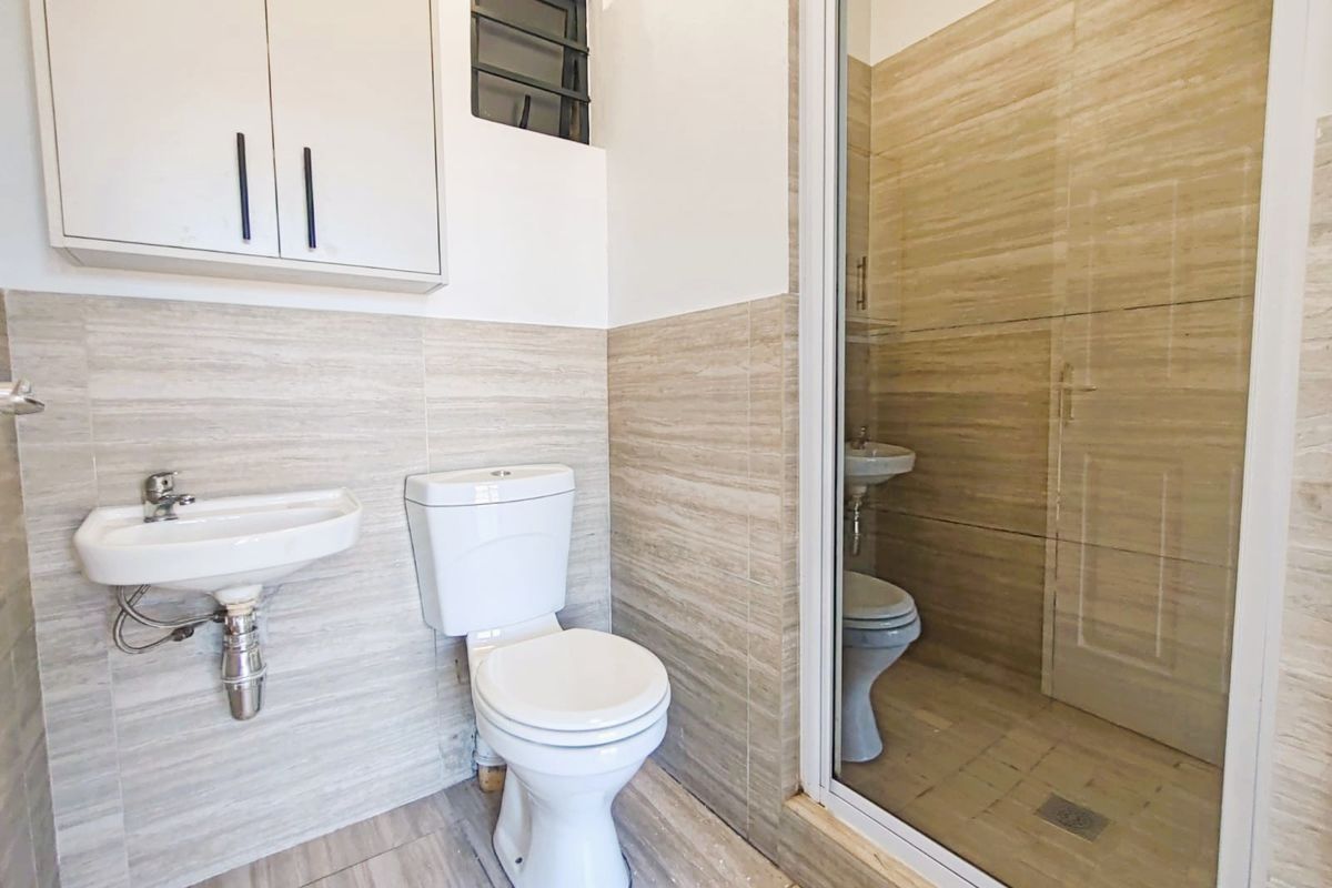 A compact bathroom featuring a wall-mounted basin, toilet, and a separate shower enclosure with neutral tiled finishes throughout.