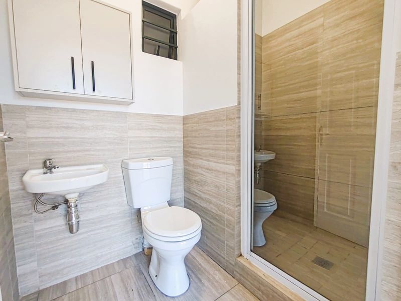 A compact bathroom featuring a wall-mounted basin, toilet, and a separate shower enclosure with neutral tiled finishes throughout.