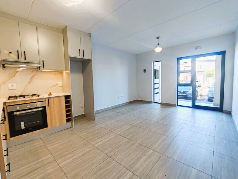 Modern open-plan kitchen and living area featuring sleek cabinetry, built-in appliances, tiled flooring, and direct access to the exterior through a glass door.