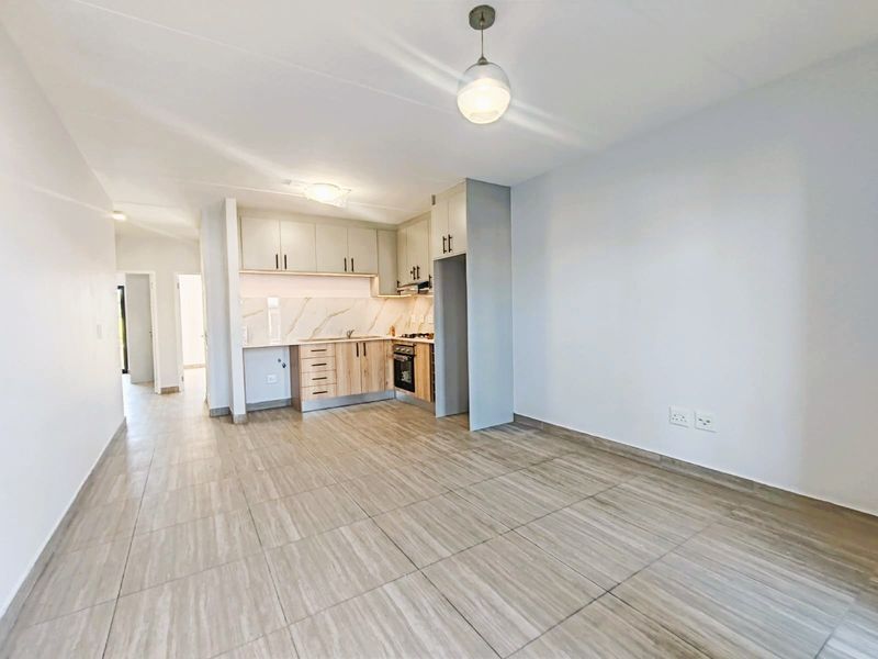 A bright, modern open-plan living and kitchen area featuring contemporary cabinetry, integrated appliances, and neutral tiled flooring throughout.