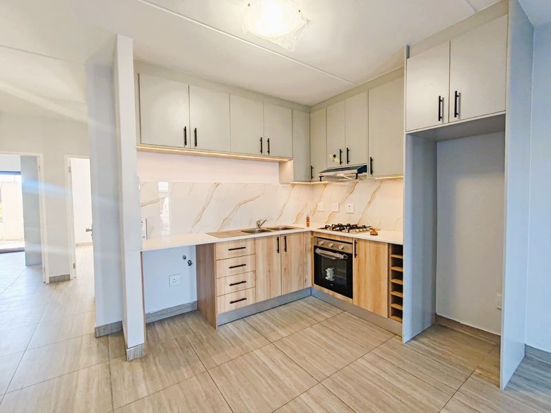 Modern kitchen featuring light wood and neutral cabinetry, stone countertops, marble-effect splashback, built-in oven, gas hob, and integrated extractor fan.