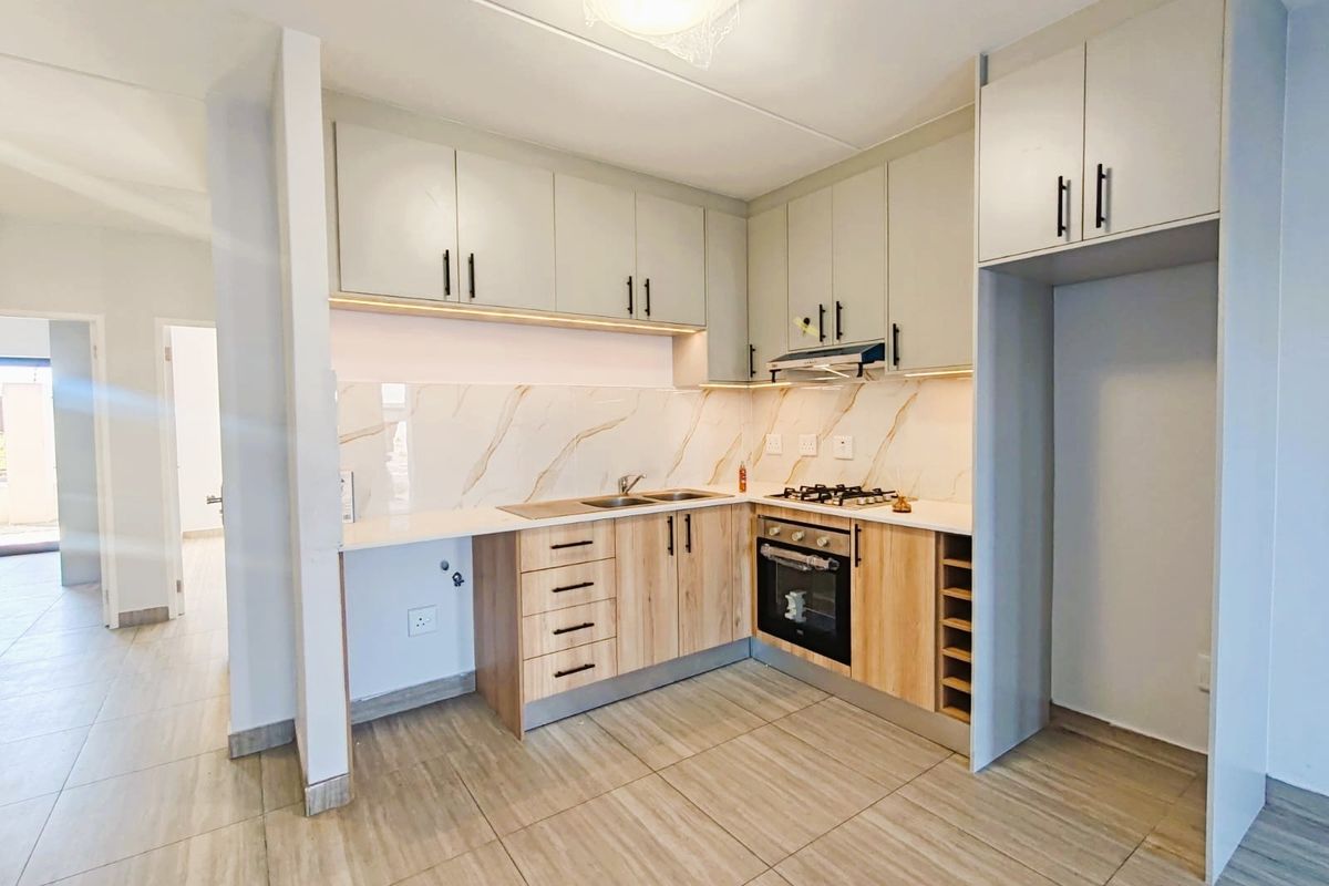 Modern kitchen featuring light wood and neutral cabinetry, stone countertops, marble-effect splashback, built-in oven, gas hob, and integrated extractor fan.