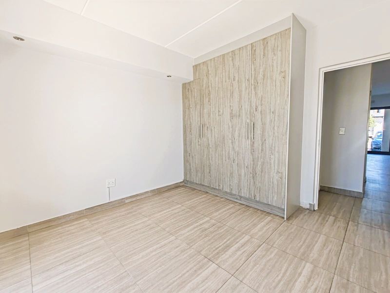 A bright, empty bedroom featuring modern wood-look built-in cupboards and neutral tiled flooring, offering a clean and versatile space.