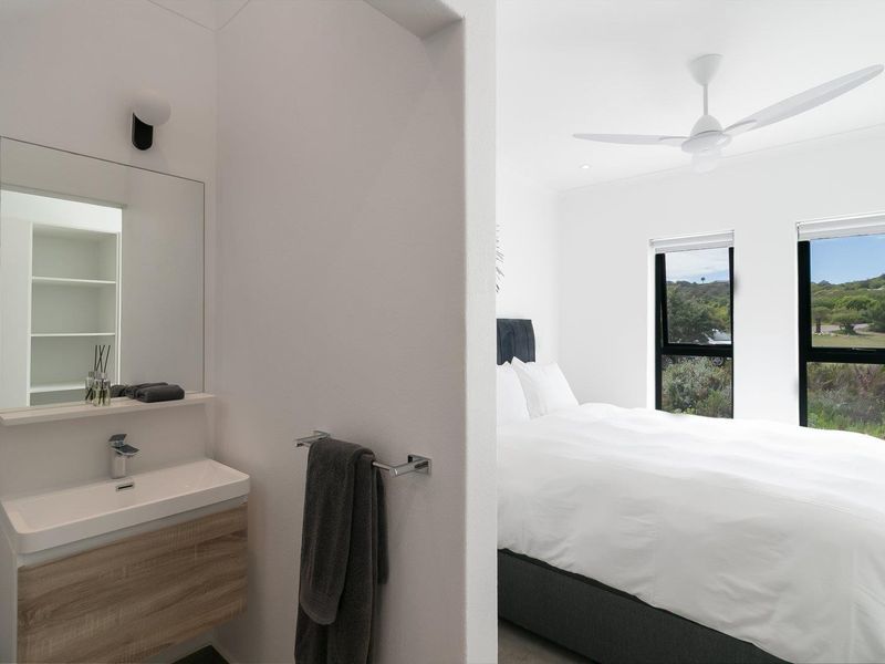 A modern bedroom featuring an integrated vanity area, contemporary basin, ceiling fan, and large windows offering scenic views.