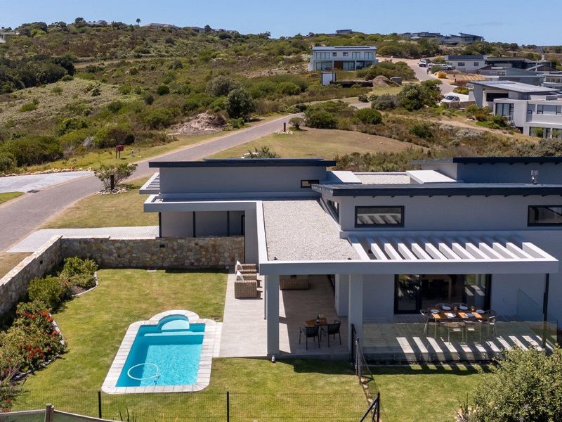 Aerial view of a modern residence featuring a swimming pool, covered patio with pergola, and landscaped garden in a coastal estate setting.