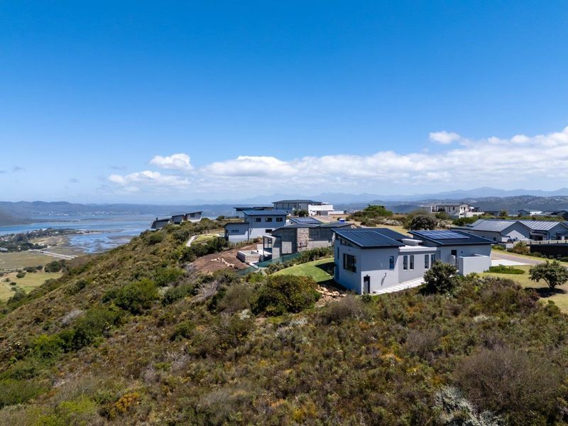 Aerial view of a modern residential estate featuring contemporary homes with solar panels, set against a scenic coastal landscape.