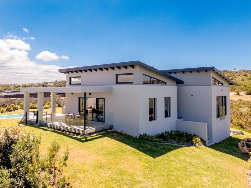 Modern rear elevation featuring a covered patio, glass balustrade, and swimming pool set within a landscaped garden.