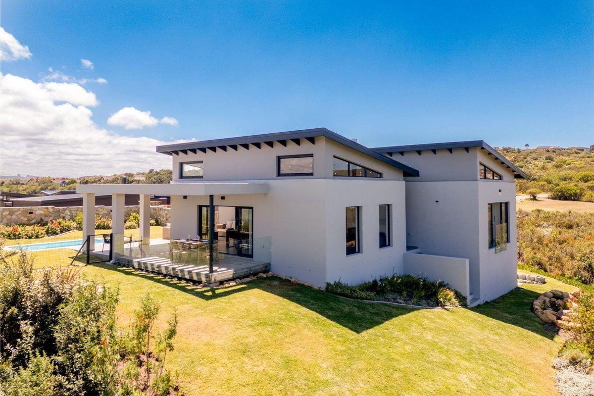 Modern rear elevation featuring a covered patio, glass balustrade, and swimming pool set within a landscaped garden.