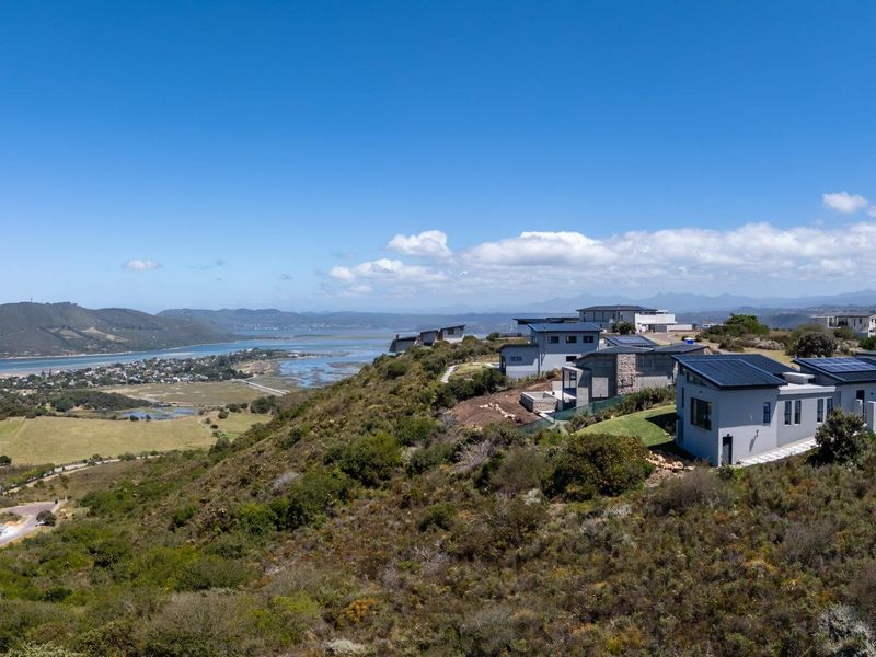 Aerial view of a modern residential estate featuring contemporary homes with metal roofs and solar panels, overlooking a scenic coastal landscape.