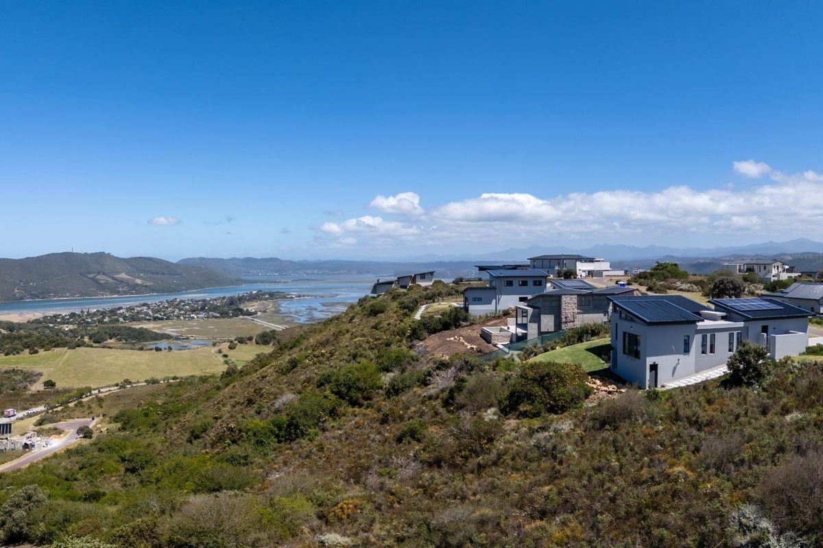 Aerial view of a modern residential estate featuring contemporary homes with metal roofs and solar panels, overlooking a scenic coastal landscape.