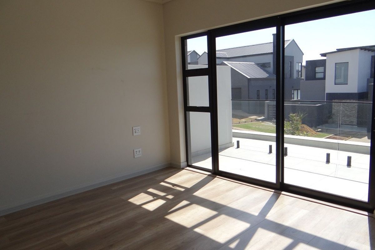 An empty bedroom featuring modern laminate flooring and large sliding glass doors that open onto a private balcony.