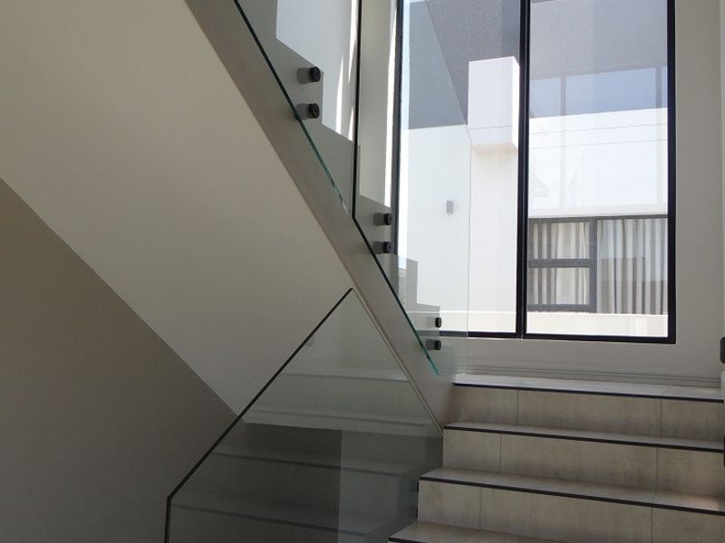 A bright, modern hallway featuring a tiled staircase with a sleek glass balustrade and a large floor-to-ceiling window providing ample natural light.